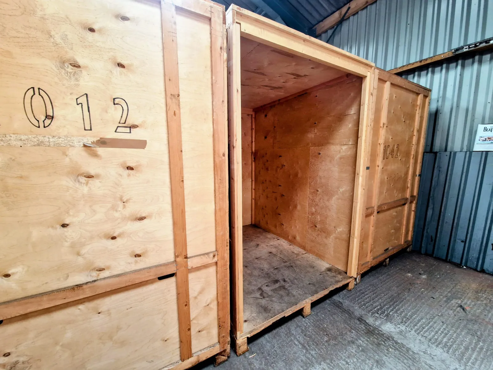 An empty 250 cubic foot wooden storage crate standing open between two closed crates